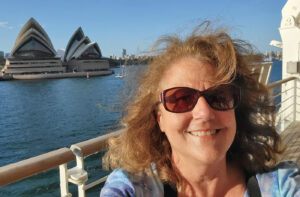 Cathy Laurenzi on a cruise ship deck with the Sydney Opera House in the background.