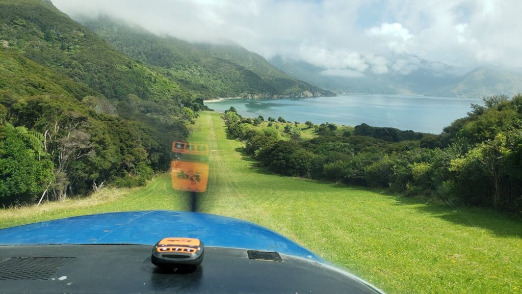 View from the cockpit of a plan taking off from a grassy landing strip in a remote area of Marlborough Sounds.