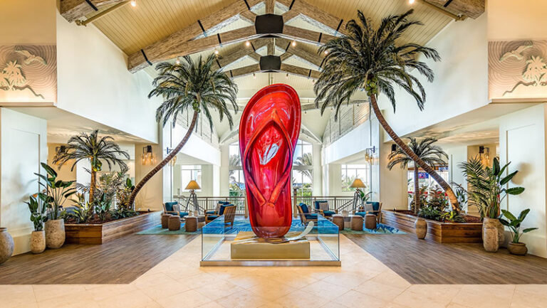 A giant red flip flop sculpture and two palm trees in a resort lobby