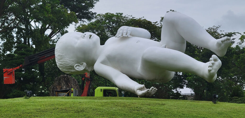 A sculpture of a giant floating baby with a crane in the background.