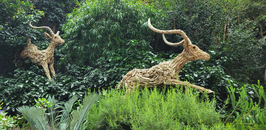 Two sculptures made of pieces of wood that are antelopes running out of the trees.