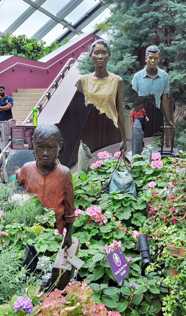 A painted bronze sculpture of a child, a man, and a woman walking with suitcases, but they have no mid-section.