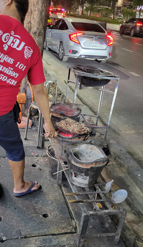 A man grilling meat over pots along side a road in Bangkok