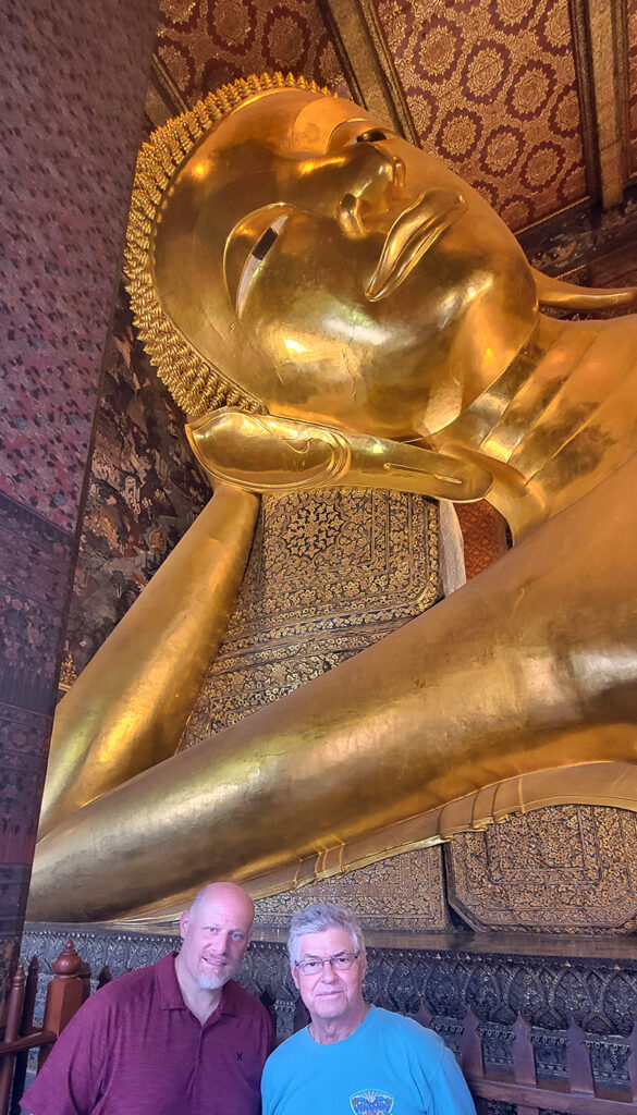 Head of Wat Pho's reclining buddha with 2 men in the foreground.