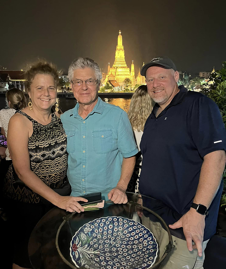 Cathy, Mark and Will posing with a view of a lit up temple in the background.