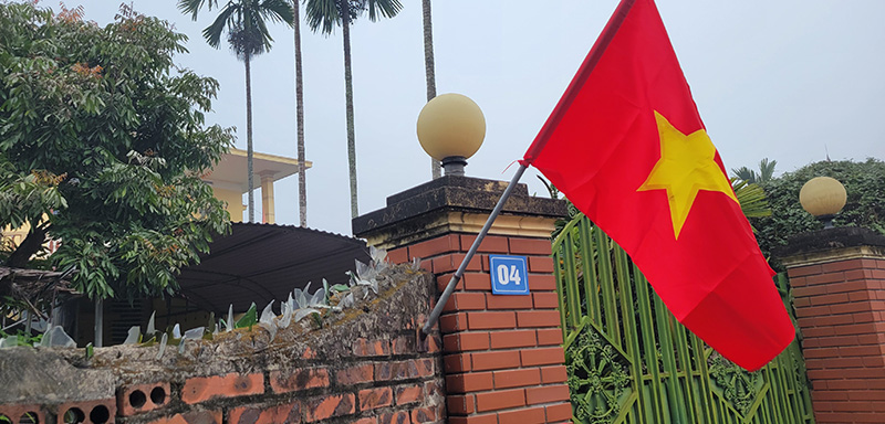 Shards of glass on top of a brick wall surrounding a home with the Vietnamese flag flying