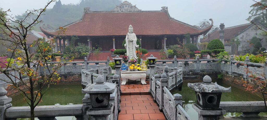 Lady buddha surrounded by small ponds with temple in the background