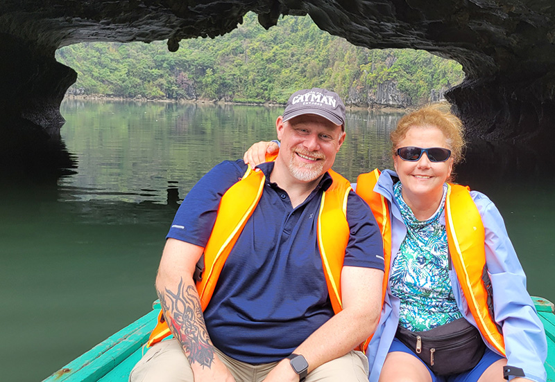 A man and a woman in a row boat with an opening in the rock behind them in the shape of the bat cave. Halong Bay, Vietnam