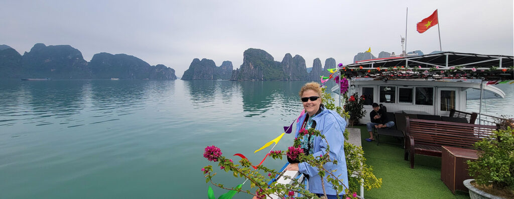 Cathy standing on the top deck of the tour boat with Ha Long Bay in the background.