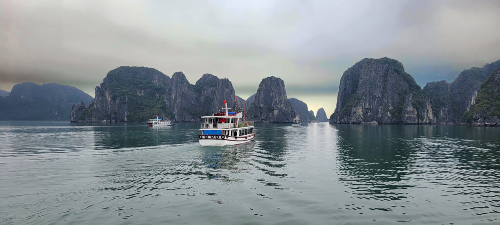 Ha Long Bay scene on a cloudy day with a boat cruising by the rock formations