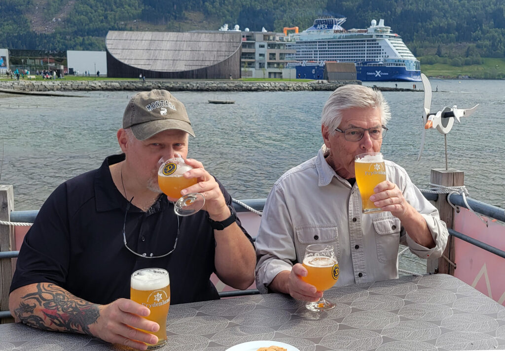 Two guys drinking two beers each in Nordfjordeid, Norway with the cruise ship Celebrity Apex in the background.