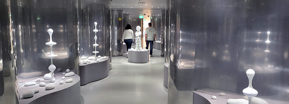 A futuristic-looking hallway on the Celebrity Apex that has wavy metal walls and rock sculptures that appear to be balancing precarously.