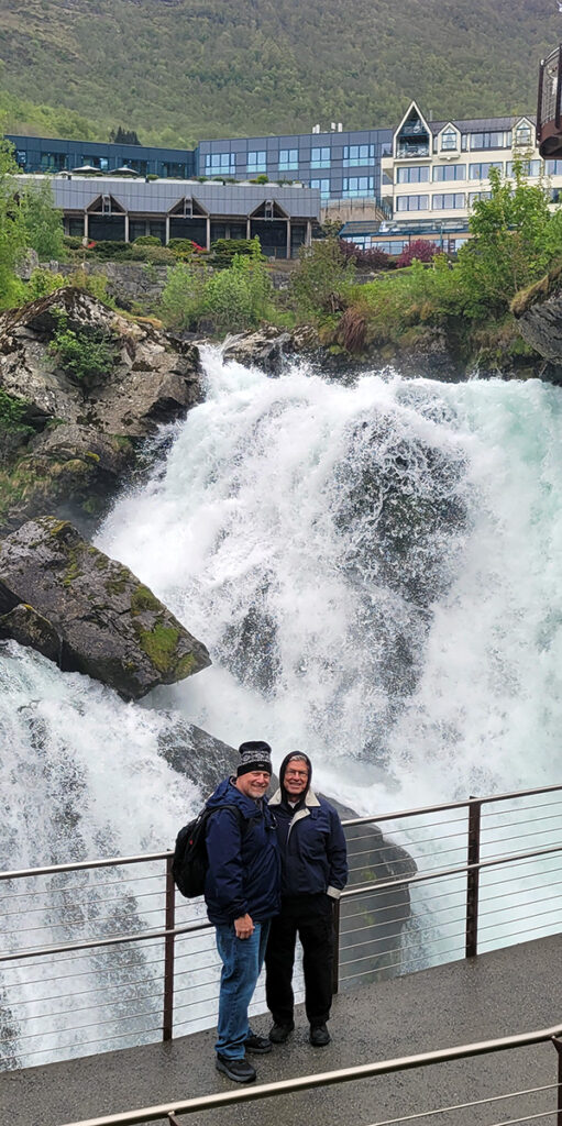 Two men standing in front of a waterfall in Geiranger, Norway