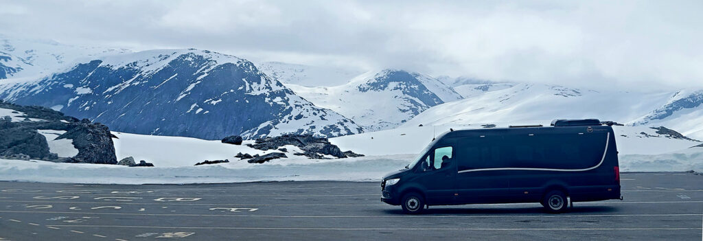 Minivan parked at Dalsnibba viewpoint in Norway with deep snow in background.
