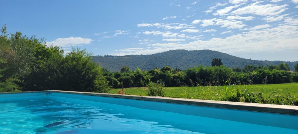 Photo is taken from a swimming pool with water in the foreground and green hills in the background.
