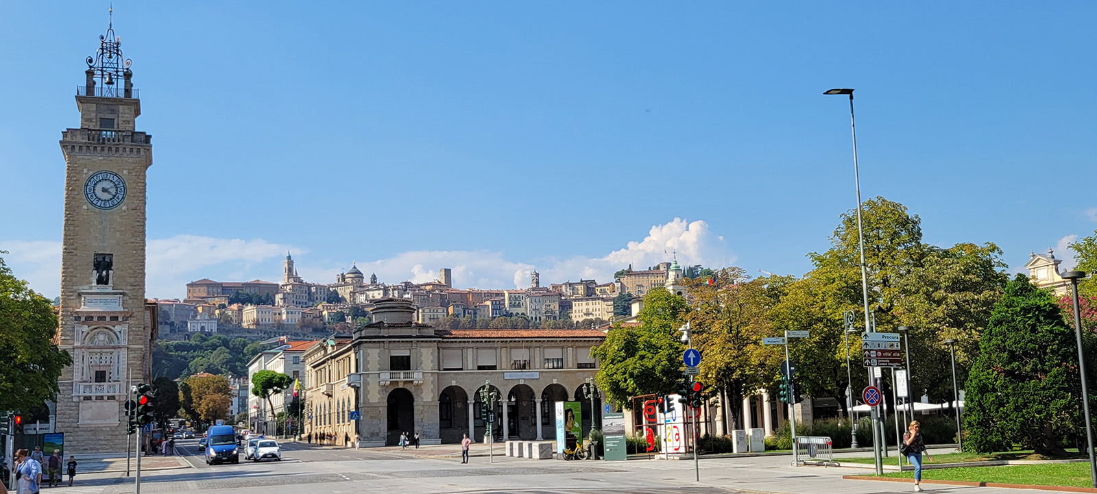 View from a street of an old building and a clock tower with the old city sitting atop a hill in the background