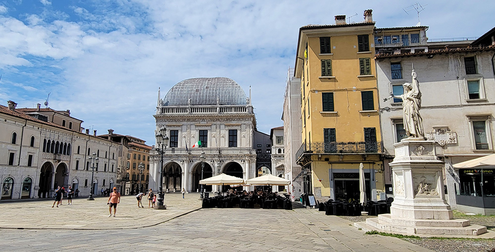 A view across the Piazza della Loggia with a statue (Monumento Bella Italia) on the right and the palace at the end of the piazza.