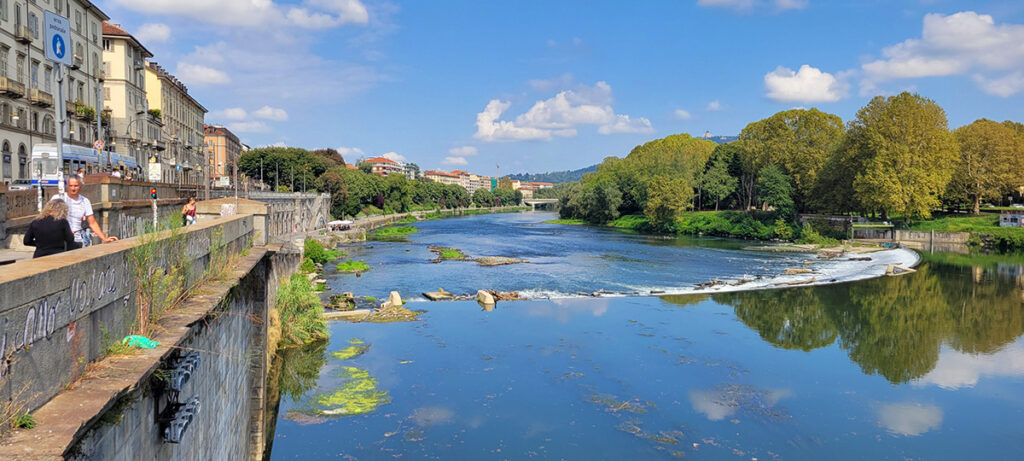 View looking up the Po river in Turin. Buildings are on the left hand side and trees on the right hand side.
