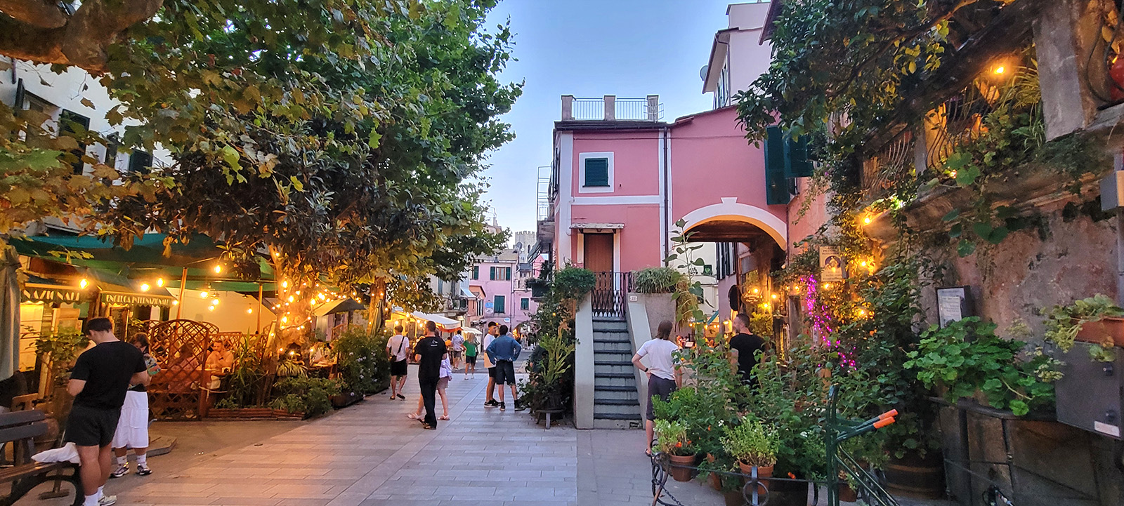 Just after dusk in an Italian town (Monterosso al Mare), people are walking in a small, uncrowded piazza, and strung lights are glowing.