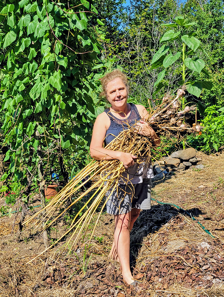 a woman holding stalks of garlic that were just pulled out of the ground