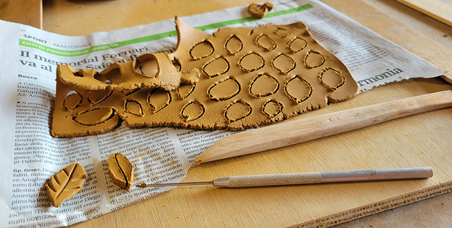 a piece of rolled out clay with leaf shapes cut into it and complete leaves in the foreground.