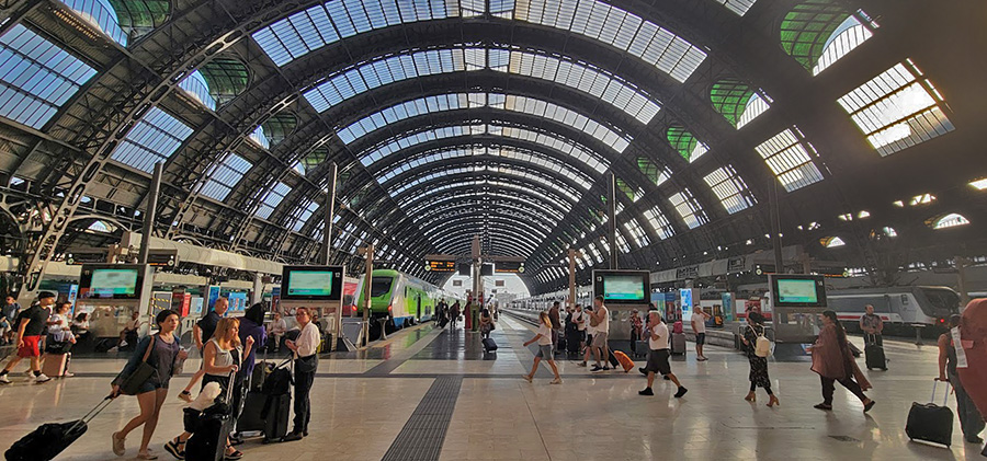 A large train station with an arched ceiling and many people walking with their luggage.