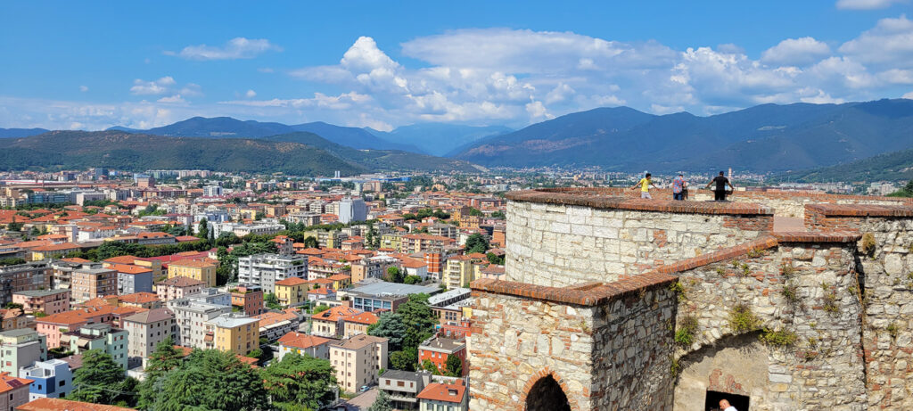 A view over the city of Brescia with people standing on a lookout on the castle walls.