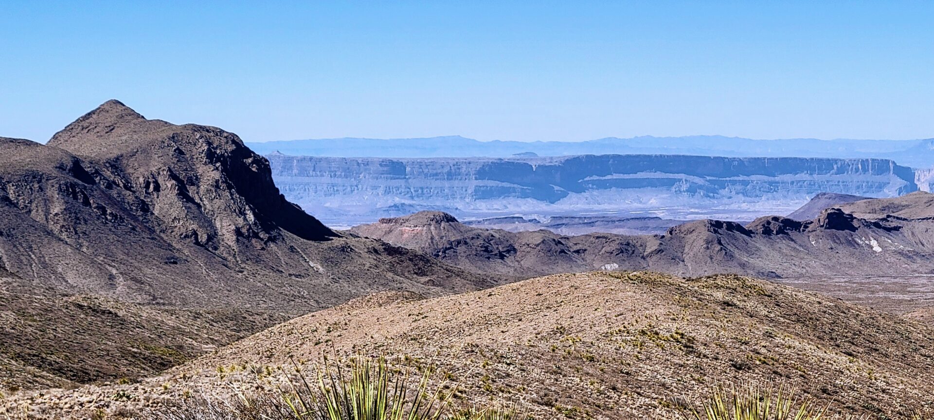 Expanse views of a desert and a flat rock face in the distance.