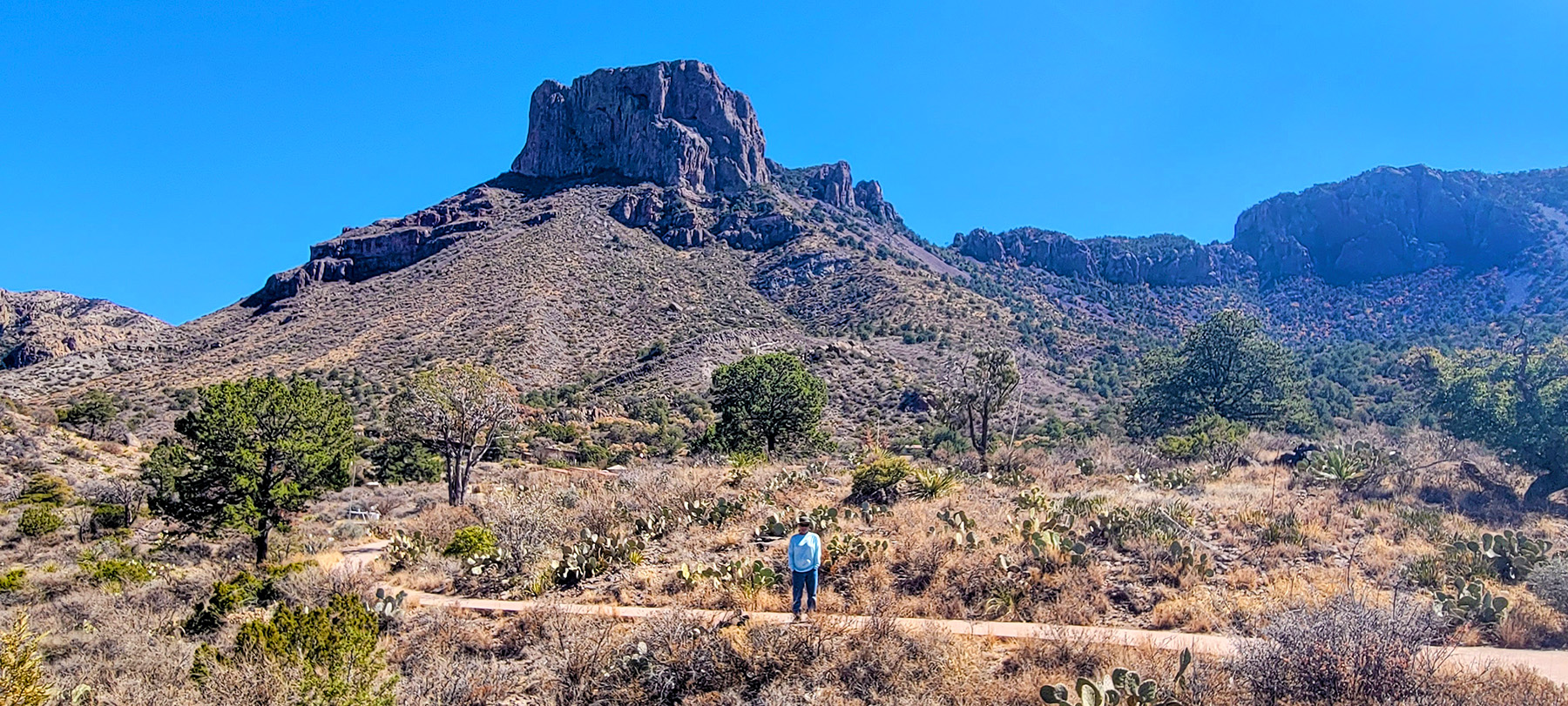 A man in the distance standing on a trail with scenic rocks behind him.