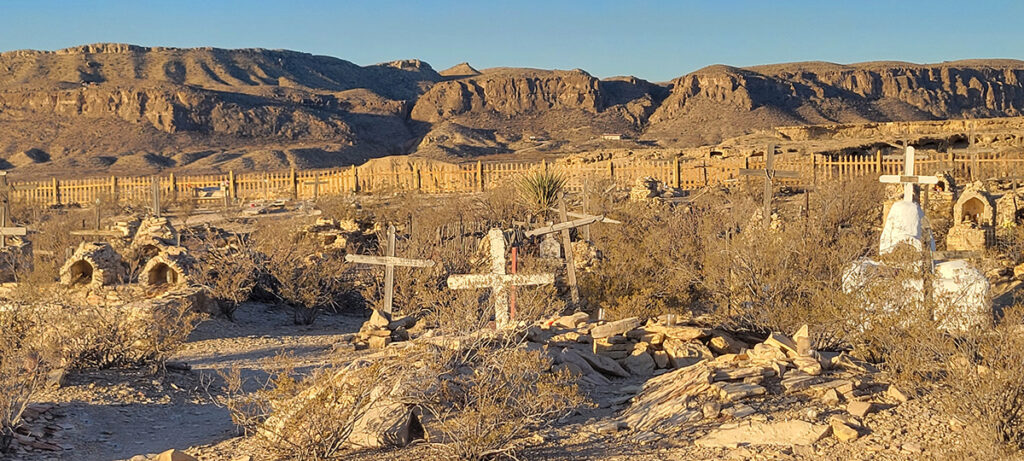 An old West cemetary with 3 rustic wooden crosses in the center of the photo.