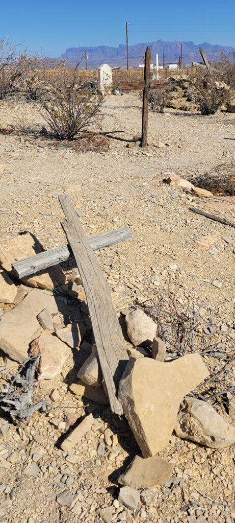 A wooden cross lying on the ground on top of some rocks in a dessert cemetary