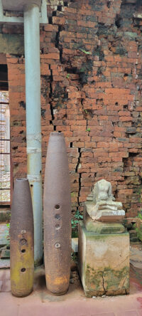 Bomb casings in front of a damaged brick wall in the My Son Sanctuary.